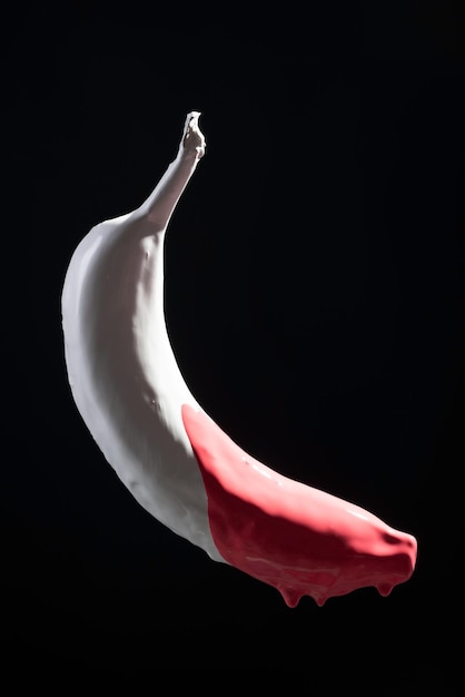 Foto rote farbe, die von der spitze einer weißen bananenschwebe auf schwarzem hintergrund haftet