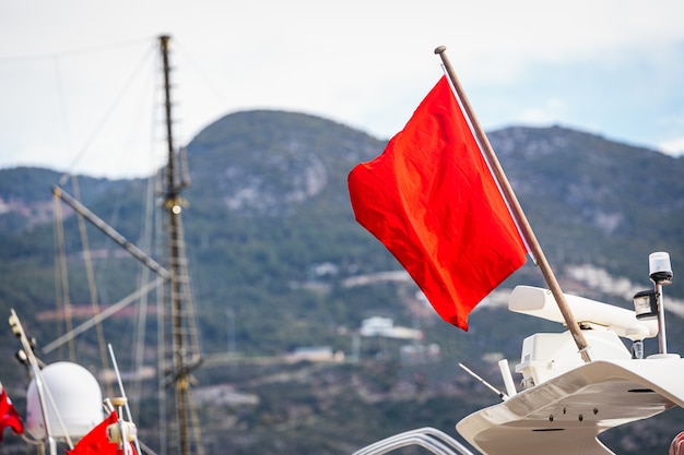 Rote Flagge weht an einer weißen Yacht vor dem Hintergrund des Jachthafens und des Meeres