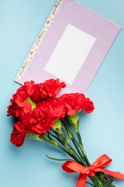 Rote Gartennelke und rosafarbener Papierumschlag mit Platz für Text auf Draufsicht des blauen Hintergrundes