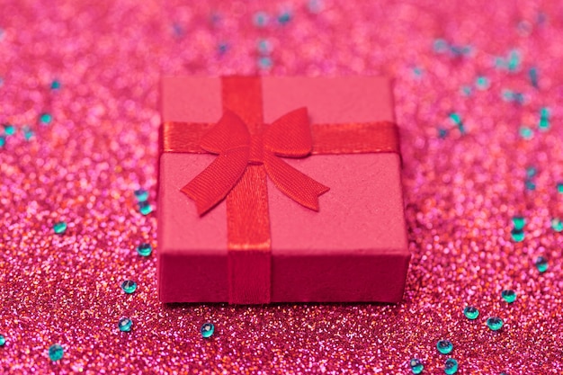 Rote Geschenkbox auf festlichem Glitzer. Kleine geschlossene Schachtel mit Schleife und Geschenk zum Jubiläum oder zur Hochzeit. Überraschungsgeschenkbox für einen lieben Menschen.
