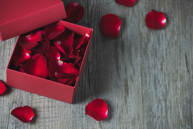 Foto rote geschenkbox mit rosenblättern im inneren, platziert auf einem grauen holzboden, draufsicht und kopierraum, valentinstagsthema