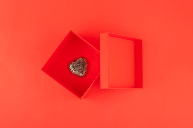 Rote Geschenkbox und ein Metallherz im Inneren auf rotem Grund