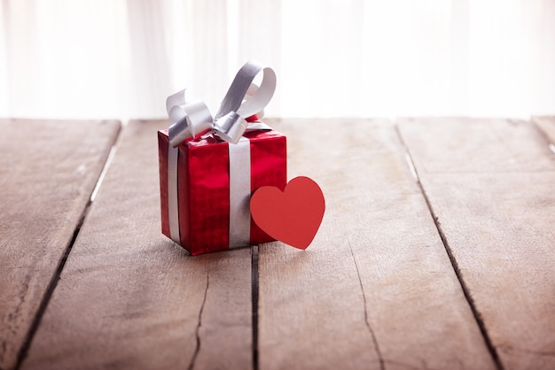 Rote Geschenkbox und Herz auf weißem Holztisch