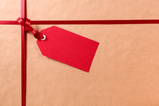 Foto rote geschenkmarke und -band, brauner paketpackpapierhintergrund, kopienraum.