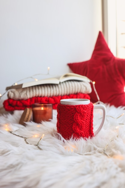 Rote gestrickte Tasse mit einem Getränk auf Weihnachtshintergrund. Wohnkomfort zum neuen Jahr