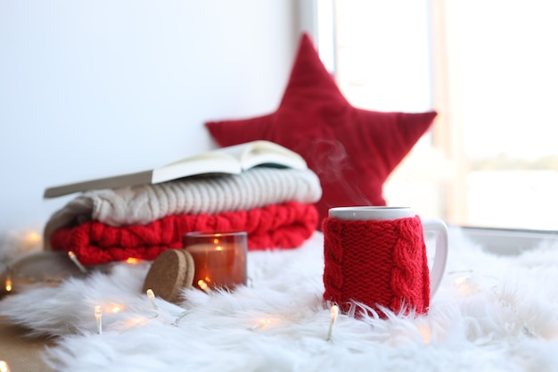 Rote gestrickte Tasse mit einem Getränk auf Weihnachtshintergrund. Wohnkomfort zum neuen Jahr