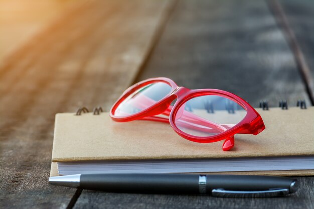 Foto rote gläser auf notizbuch mit stift-und holz-hintergrund