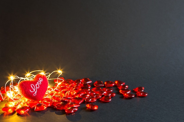 Rote Glasherzen und weiches Plüschherz mit den Worten Liebe auf schwarzem Hintergrund, goldene Lichter - Valentinstag. Urlaub, Banner, Copyspace. Einkaufen und präsentieren, Geschenk für einen geliebten Menschen, verliebtes Paar