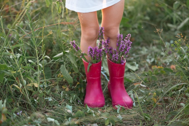 Foto rote gummistiefel an den füßen eines mädchens mit einem strauß wilder blumen blumen in einem stiefel sommer sommer freiheit natur landschaft grünes gras auf dem feld