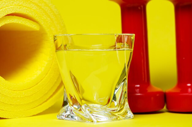 Rote Hanteln, ein Glas Wasser, ein gelber Teppich, farbiger Hintergrund, Sport, Energy-Drink, Geräte für das Fitnessstudio