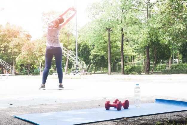 Rote Hanteln und Flasche Wasser auf Yoga-Matte, Frau Ausübung im Hintergrund