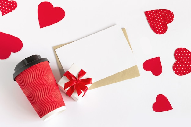 Rote Herzen, eine rote Tasse Kaffee, eine Geschenkbox, ein weißes Blatt Papier und ein Brief