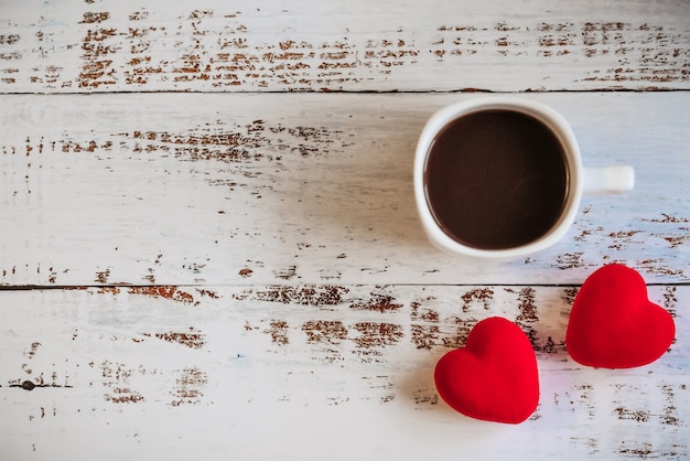 Rote Herzen und eine Tasse Kaffee auf einem weißen hölzernen Hintergrund.