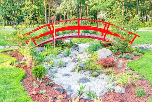 Rote japanische Brücke über schönem Blumenbeet im grünen Park