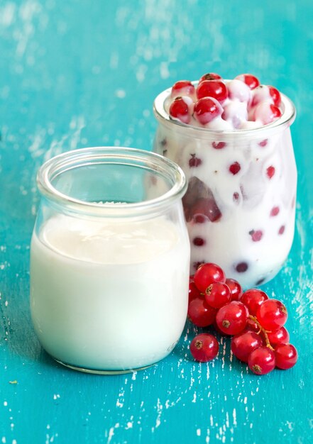 Rote Johannisbeeren und frischer Joghurt in einem Glas auf türkisfarbenem Holztisch schließen oben