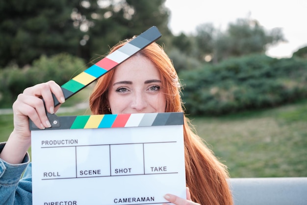 Foto rote junge frau mit blauen augen, bedeckt mit einem film-clapperboard, konzept-lebensstil-kino-augen