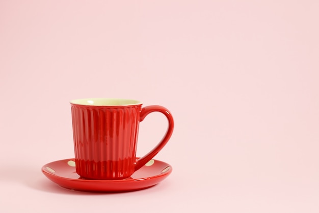 Rote Kaffeetasse auf roter Platte über rosa Hintergrund.