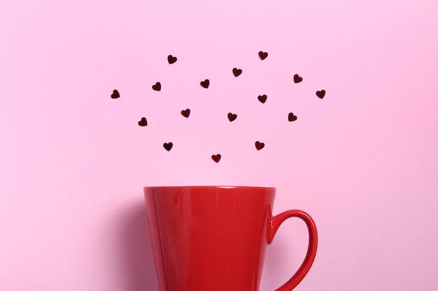 Rote Kaffeetasse mit roten Funkelnherzen auf rosa Wand. Flache Laienzusammensetzung. Romantisch, St. Valentinstag-Konzept.