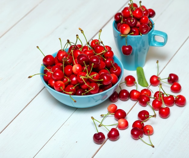 Rote Kirschen in einer schönen blauen Schüssel auf weißem Holzhintergrund