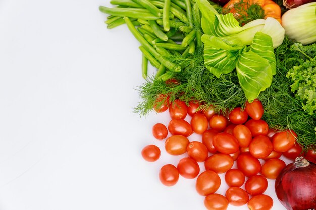 Rote Kirschtomaten, grüne Erbsen und Dill auf weißem Tisch.