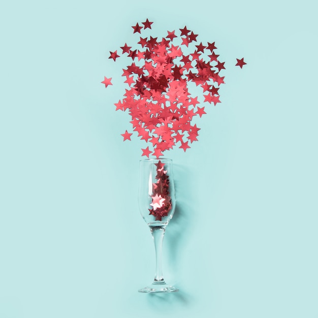 Rote Konfetti in Form von Sternen gossen Gläser Champagner auf Blau aus.