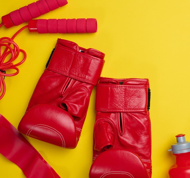 Rote Lederboxhandschuhe Wasserflasche Sportgeräte auf gelbem Hintergrund