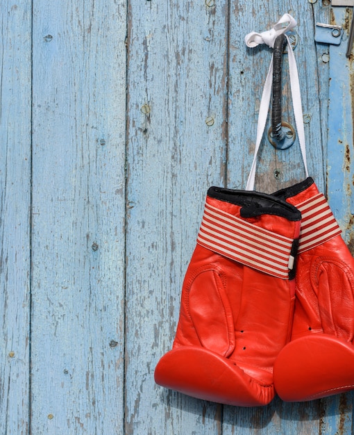 Rote lederne Boxhandschuhe, die an einer alten blauen hölzernen Wand hängen