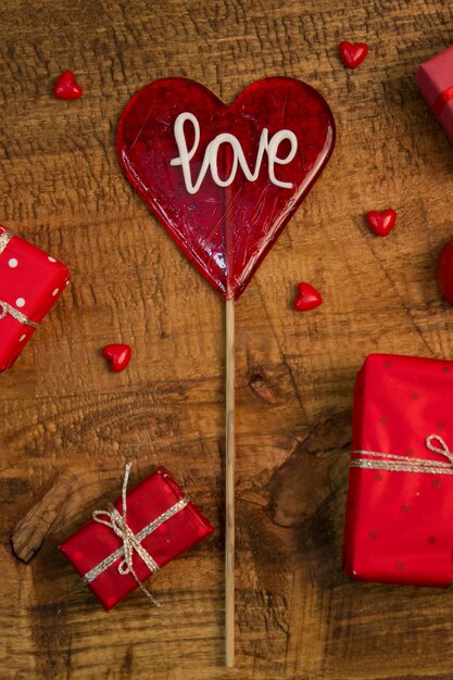 Foto rote liebe lollipop, geschenke und mini-glas herzen auf holztisch. valentines dekoration