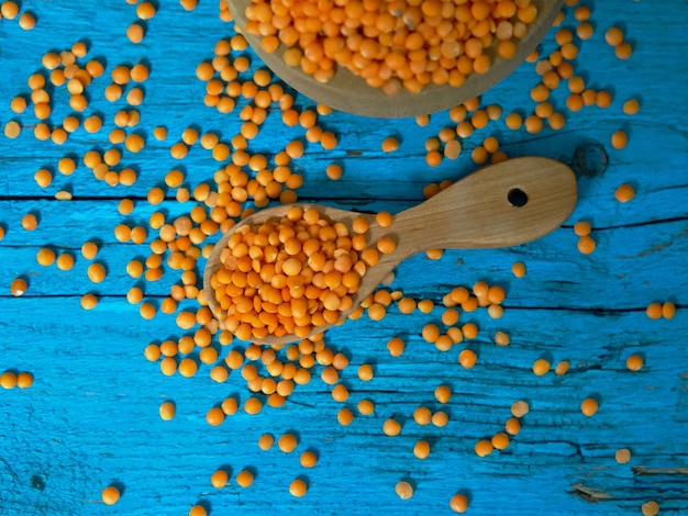 Rote Linsen in einer Holzplatte und einem Löffel auf einem alten rustikalen Tisch. Vegetarisches Essen.