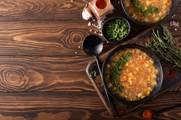 Rote Linsen-Mais-Suppe mit Kräutern und Paprika in einer schwarzen Schüssel auf einem Holztisch