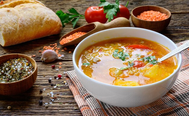 Rote Linsensuppe auf dem rustikalen Holztisch mit Gemüse, Gewürzen und selbstgebackenem Brot.