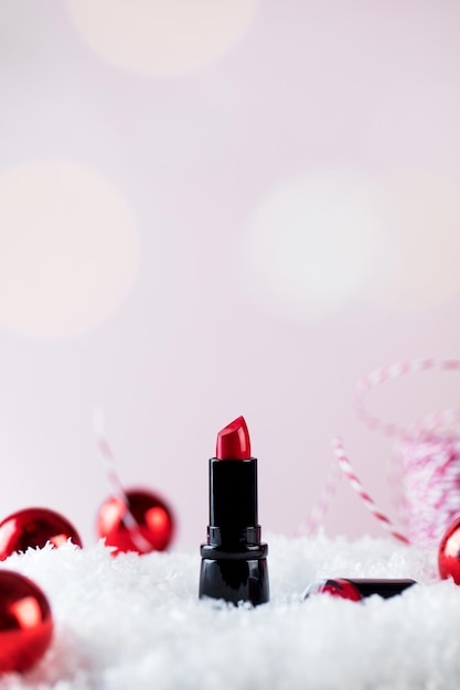 Foto rote lippenstiftröhre und weihnachtsbaumkugeln auf künstlichem schneehaufen