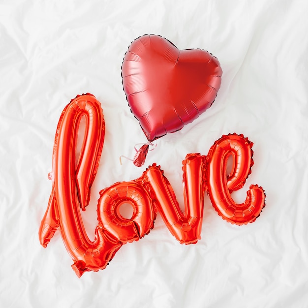 Rote Luftballons in Form des Wortes "Love" mit Herzen auf dem Bett. Liebe Konzept. Urlaub, Feier. Valentinstag oder Hochzeits-/Junggesellinnenabschiedsdekoration. Folienballon