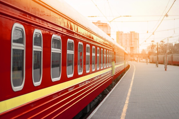 Rote Metallzugbahnwagen mit Fenstern auf einem Bahnsteig im Sonnenuntergangslicht.