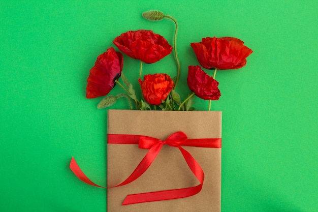 Rote Mohnblumen in einem Umschlag mit einem roten Band auf dem Grün gebunden