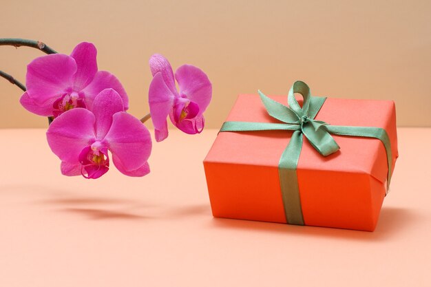 Rote orchideenblüten mit geschenkbox auf beigem hintergrund.