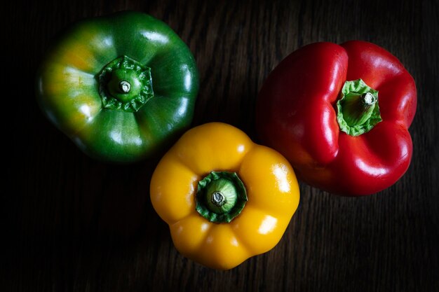 Rote Paprika grüne Paprika und gelbe Paprika auf Holztisch und dunklem Hintergrund