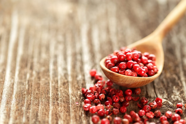 Rote Pfefferkörner in einem Löffel auf Holztisch