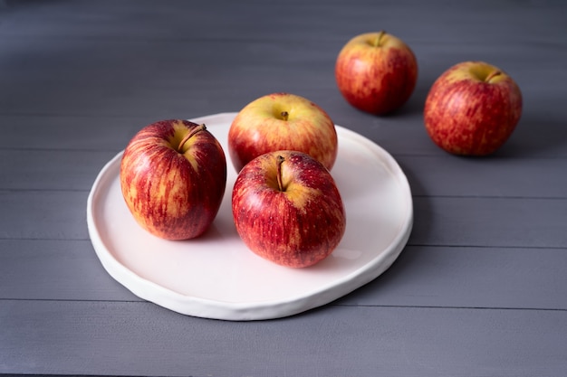 Rote Äpfel auf flachem weißen Teller handgefertigt auf einem grauen Holztisch