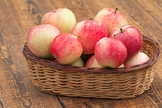 Rote Äpfel im Weidenkorb auf alten Holzbrettern