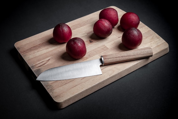 Rote Pflaumen auf Brotbrett mit Messer und schwarzem Hintergrund