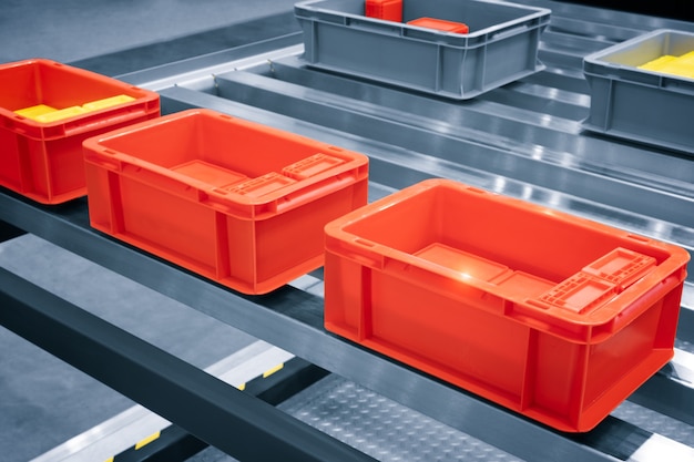 Rote Plastikbox auf Rollenlinie für den Transfer von Produktionsteilen in der Produktionslinie in Fabrik, Produktion, Transportkonzept