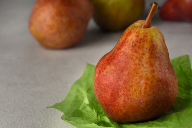 Rote reife Birnen auf hellem Hintergrund. Birne auf einem Stück zerknittertem grünem Geschenkpapier und drei Birnen auf Hintergrund.