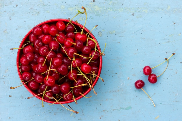 Rote reife Kirschen mit Endstücken in einer Kreisplatte auf einem alten blauen hölzernen Hintergrund. Draufsicht der Nahaufnahme