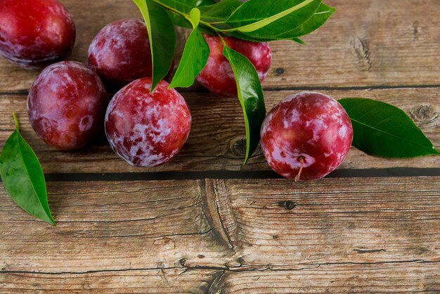 Rote reife Pflaume mit grünen Blättern auf hölzernem Hintergrund.