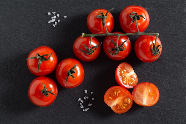 Foto rote reife tomaten und großes meersalz auf schwarzem hintergrund