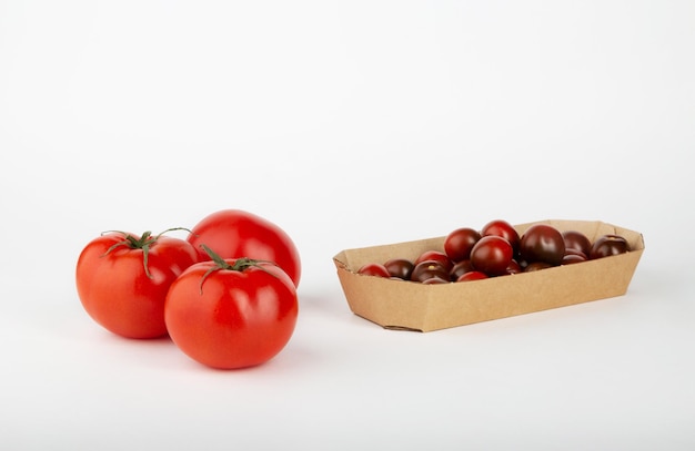 Rote reife Tomaten und kleine Kirschtomaten in einer Schachtel auf weißem Hintergrund