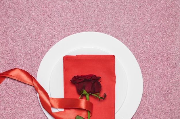 Rote Rose mit Band auf Platte auf rotem Hintergrund. Valentinstag.