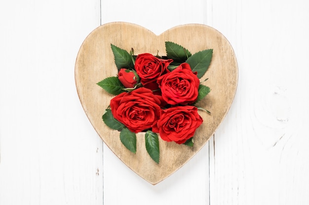Rote Rosen des Valentinstagkonzepts und hölzernes Herz auf weißem Hintergrund