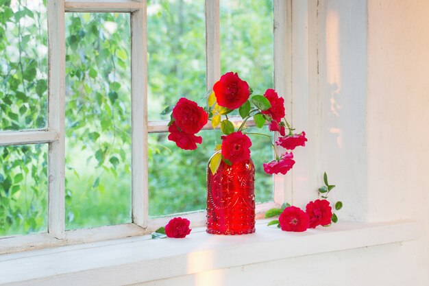 Rote Rosen in roter Glasvase auf Fensterbank